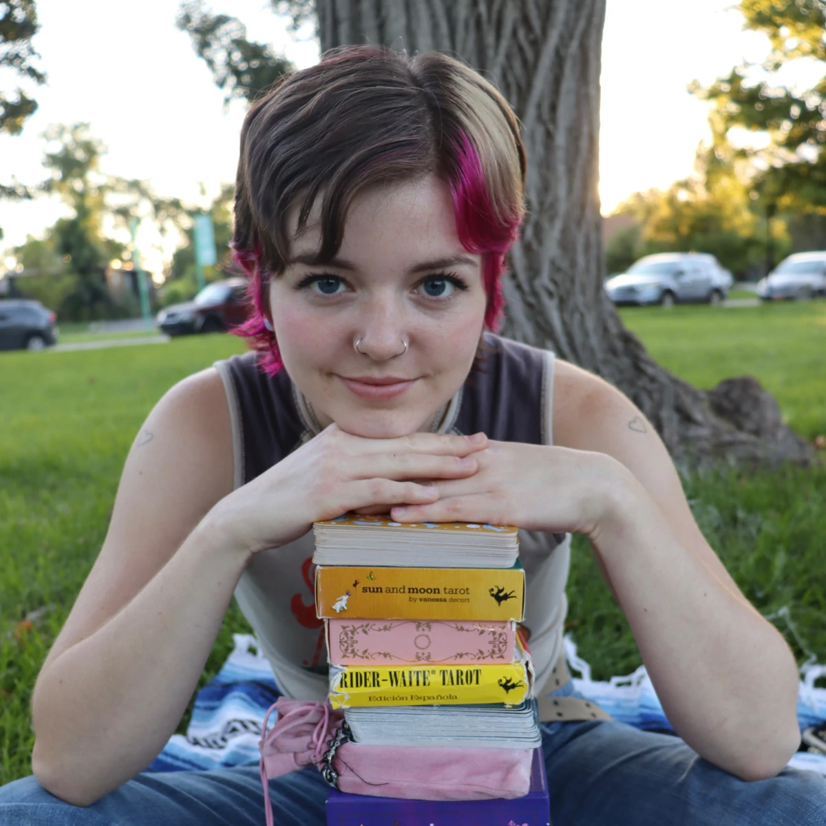 Jaylee resting her chin on her hands above a stack of tarot decks outdoors